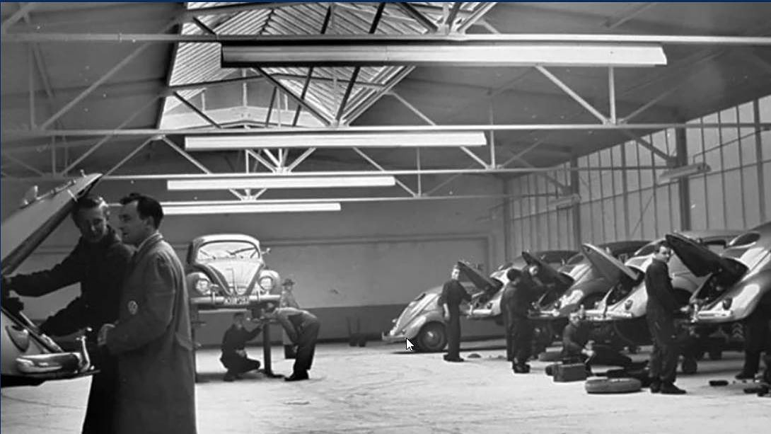 Historisches Foto unserer Werkstatt, in welcher Mechaniker an diversen VW Käfer arbeiten.